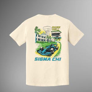 Op de afbeelding: Crèmekleurig T-shirt met een blauwe raceauto op een kronkelende weg, met een gebouw en palmbomen. De tekst "RAISE HELL" en "SIGMA CHI" is ook zichtbaar.