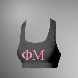 Op de afbeelding: Een donkergrijze sportbeha met een ronde hals en brede bandjes. De beha heeft de Griekse letters ΦΜ in roze op de voorkant. De achtergrond is effen grijs.