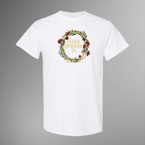 Könnte beinhalten: Weißes T-Shirt mit einem goldenen geometrischen Kranzdesign, das grüne Blätter, rote Blüten und den goldenen Text "ALPHA OMICRON PI" enthält. Das T-Shirt hat kurze Ärmel und einen Rundhalsausschnitt.