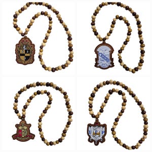 May include: Four wooden bead necklaces with different pendant designs. Each necklace features a mix of light and dark brown wooden beads. The pendants have various crests and symbols, with some including text. The necklaces are displayed against a white background.