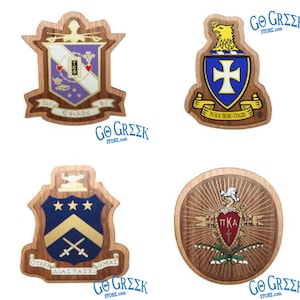 Może przedstawiać: Cztery drewniane plakietki z herbami greckich bractw i stowarzyszeń. Herby mają różne kształty i kolory, w tym niebieski, złoty, fioletowy i biały. Na każdej plakietce znajduje się napis "GO GREEK STORE.com".