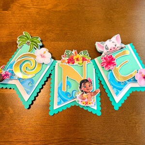 May include: A banner with three pennants featuring a tropical theme. Each pennant has a teal background with gold lettering and tropical flowers. The banner includes images of a palm tree, a pig, and a young girl.