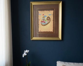 May include: A framed artwork with a gold-colored frame hangs on a dark blue wall. The artwork features a colorful illustration with a gold background. A white orchid in a white pot sits on a wooden side table.