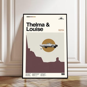 Puede incluir: Un póster enmarcado con el título de la película "Thelma & Louise" en negro. El diseño incluye un gráfico de coche clásico sobre un círculo beige, con un paisaje burdeos debajo. El año 1991 se muestra en la parte inferior.