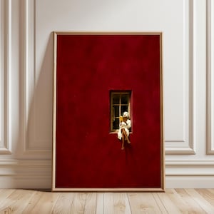 May include: A framed vertical wall art print featuring a deep red wall with a single rectangular window. A person wearing a white bathrobe and a matching head towel sits on the window ledge, reading a yellow book. The frame is light wood.