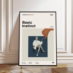 May include: A framed poster featuring the text "Basic Instinct" in bold black letters. The poster includes an image of a woman in a white coat, seated on a chair. The poster has a neutral color palette with a touch of orange.