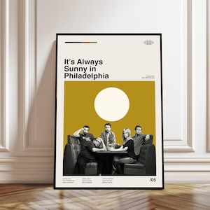 May include: A framed poster featuring the text "It's Always Sunny in Philadelphia" above a group of people seated at a table. The poster has a cream background with a large white circle and a mustard yellow section. The bottom right corner has the number "/05".