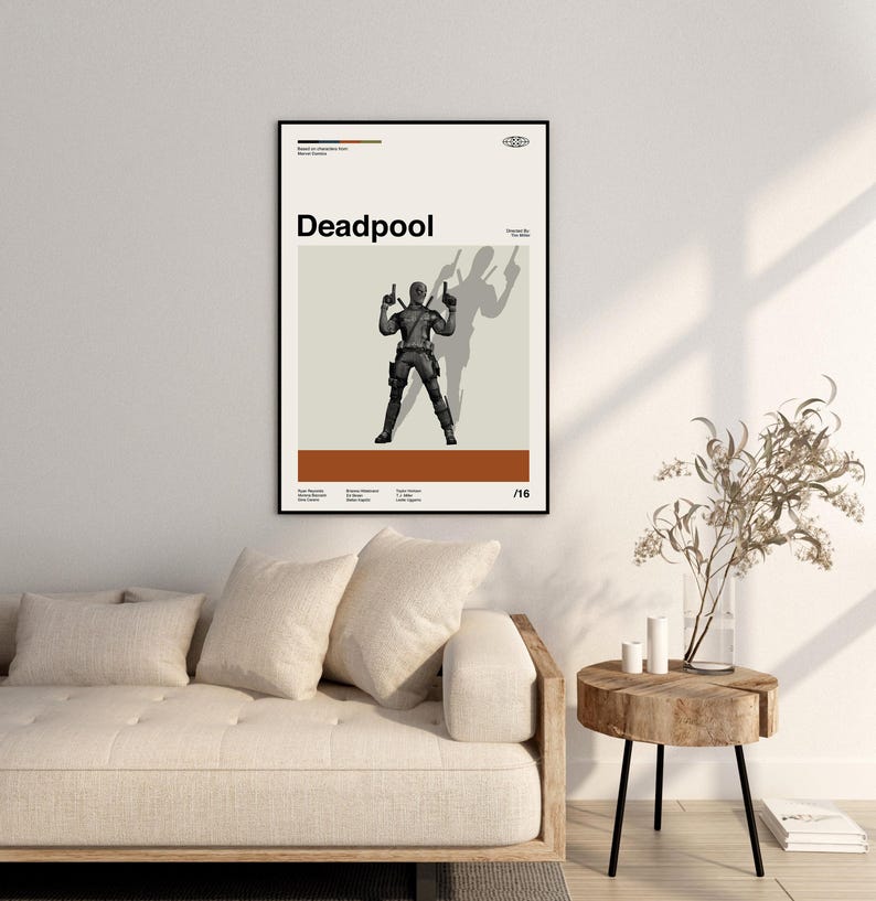 Puede incluir: Un p&oacute;ster enmarcado con la palabra "Deadpool" en negro. El p&oacute;ster muestra una figura con un traje negro con armas levantadas, proyectando una sombra. El fondo es beige y marr&oacute;n. El p&oacute;ster se muestra en una pared blanca.