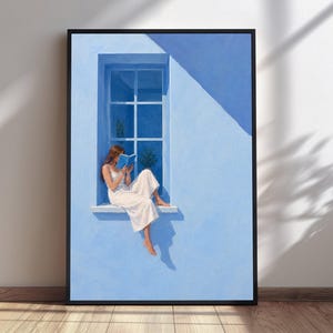 May include: A framed wall art print depicting a person in a white dress sitting on a window ledge of a light blue building. The person is reading a blue book. The scene features a multi-pane window, sharp shadows, and a bright, monochromatic blue color palette.