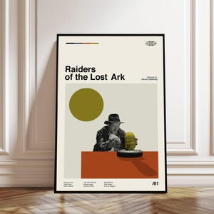 May include: A framed poster featuring the movie title "Raiders of the Lost Ark." The poster has a minimalist design with a color block background, a large yellow circle, and an image of a man in a hat. The poster includes the director's name and cast credits.