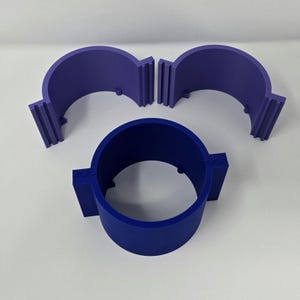 May include: Three blue and purple plastic objects. One is a complete cylinder, and the other two are semi-circular pieces. The pieces have a ridged design on the edges and are likely components of a larger item.