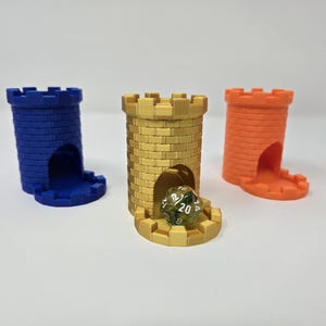 May include: Three colorful dice towers in blue, gold, and orange, each resembling a castle turret. The gold tower holds a multi-sided die. These 3D-printed towers are designed for tabletop gaming.