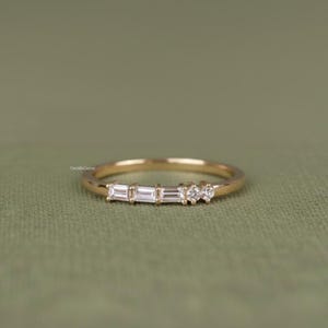 Op de afbeelding: Een delicate gouden ring met drie rechthoekig geslepen edelstenen en twee kleine ronde stenen. De ring is gezet op een dunne gouden band. De edelstenen zijn helder en sprankelend. De ring ligt op een groene achtergrond.