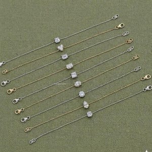 May include: A collection of delicate bracelets with various gemstone shapes, including heart, emerald, and pear cuts. The bracelets feature a mix of silver and gold chains, each with a clasp closure. The gemstones are set in a minimalist style, creating an elegant look.