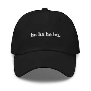 May include: Black baseball cap with a curved brim. The cap features the embroidered text "ha ha he hu." in white, centered on the front. The cap has a classic six-panel design with a button on top.