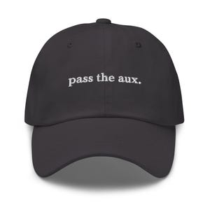 May include: A dark grey baseball cap with a curved peak. The phrase "pass the aux." is embroidered in white across the front. The cap has a structured fit and a top button.