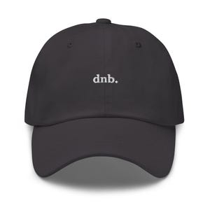 Puede incluir: Gorra de béisbol gris oscuro con visera curva. La gorra presenta el texto "dnb." bordado en blanco en el centro. El sombrero tiene un diseño clásico de seis paneles con un botón en la parte superior.