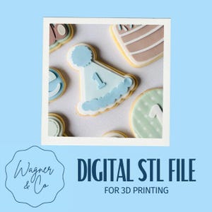 May include: A selection of decorated biscuits, including a light blue party hat-shaped biscuit with the number 1. Other biscuits feature pastel colours and designs. The image is framed with a white border and set against a light blue background.