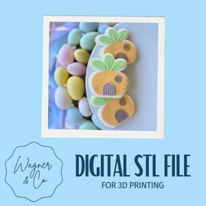 Może przedstawiać: Cyfrowy plik STL do druku 3D. Obraz przedstawia ciasteczka w kształcie marchewek z zielonymi wierzchołkami i detalami drzwi, obok pastelowych jajek wielkanocnych. Ciasteczka znajdują się na białym talerzu, z jasnoniebieskim tłem. Widoczny jest również tekst "DIGITAL STL FILE FOR 3D PRINTING".