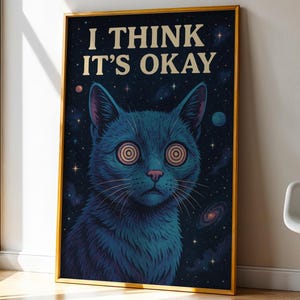 Könnte beinhalten: Ein gerahmter Kunstdruck mit einer blauen Katze mit Spiralaugen vor einem Sternenhintergrund. Der Text "I THINK IT'S OKAY" steht oben. Das Kunstwerk befindet sich in einem goldenen Rahmen, neben einem Fenster und einem weißen Stuhl.