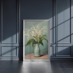以下が含まれることがあります： 白いスズランの花が飾られた、淡い緑色の花瓶の静物画が描かれた額入りのアートプリント。花瓶は、淡い緑色の背景に対して、ピンク色の表面に置かれています。アートワークは、銀色のフレームで表示されています。