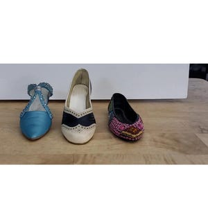 Könnte beinhalten: Drei Paar Damenschuhe werden gezeigt. Die Schuhe umfassen ein hellblaues Paar mit Riemen und Verzierungen, ein cremefarbenes Paar mit schwarzem Design und ein schwarzes Paar mit bunten Perlen.