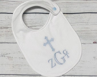 May include: White baby bib with a textured waffle weave. The bib features a light blue embroidered cross and the initials "Z G" in a script font. A light blue snap closure is at the neck.