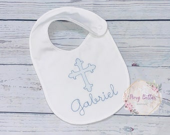 May include: White baby bib with blue embroidery of a cross and the name Gabriel.