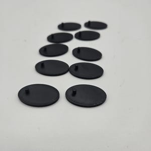 Pode incluir: Oito bases redondas de plástico preto com um pequeno pino no topo. As bases estão dispostas em um padrão escalonado.