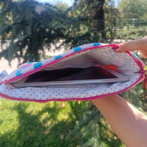 May include: A pink and white tablet sleeve with a blue polka dot pattern and a pink zipper. The interior lining is white with small purple polka dots. A tablet is visible inside the sleeve.