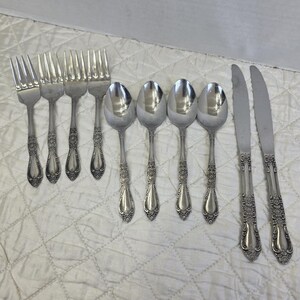 May include: A set of vintage silverware, including forks, spoons, and knives. The silverware has a shiny, silver finish with ornate floral detailing on the handles. The set includes four forks, six spoons, and two knives.