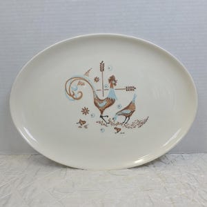 May include: An oval, off-white serving platter with a rooster and hen design. The rooster has brown and blue feathers, and the hen is brown. The design includes wheat stalks and small floral accents. The platter is a vintage piece.