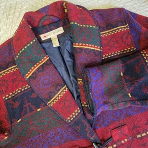 May include: A vintage wool coat with a striking pattern in red, purple, green, and gold. The coat has a notched collar, navy blue lining, and a toggle closure. The label reads "ROO CROSSING".