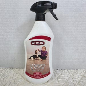 May include: White plastic spray bottle of Weiman Laminate & Stone floor cleaner. The bottle has a black spray nozzle and a red and white label with a baby and a dog. The bottle contains 27 fl oz of non-toxic and biodegradable formula.