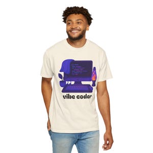 Puede incluir: Camiseta color crema con un gráfico de una computadora con código, una lámpara de lava y una planta en maceta. El texto "vibe coder" está debajo del gráfico. La camiseta la lleva una persona.