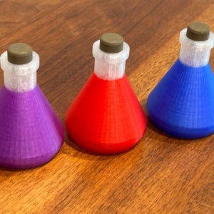 May include: Three colorful potion bottles in purple, red, and blue. Each bottle has a conical shape with a white neck and a brown cap. The bottles are arranged on a wooden surface.