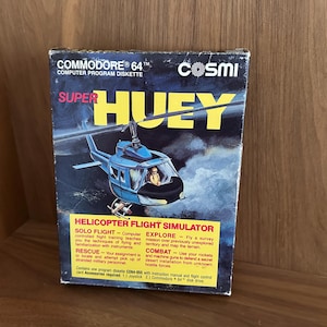 May include: A vintage Commodore 64 Super Huey helicopter flight simulator game box. The box features a blue helicopter illustration with yellow text. The game includes solo flight, explore, rescue, and combat modes.