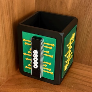 May include: Black and green square desk organizer with a circuit board design. The front features the number "68000" in white. The sides have yellow and green accents, creating a tech-inspired aesthetic.