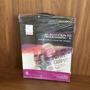 May include: Sealed Atari 400/800 computer program cassette titled "An Invitation to Programming 3: Introduction to Sound and Graphics." The box features a portrait and colorful graphics. The Atari logo is visible.