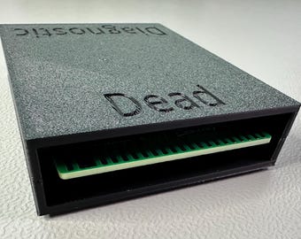 Può includere: Una scatola nera con le parole "Diagnostic" e "Dead" stampate sulla parte superiore. La scatola ha una fessura per una scheda di circuito, che è visibile all'interno della scatola.