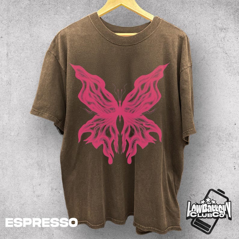 Może przedstawiać: Koszulka w kolorze espresso z wyrazistą r&oacute;żową grafiką motyla. Koszulka ma wygląd vintage i prany, z luźnym krojem. Tekst "ESPRESSO" znajduje się na dole. Logo "Low Battery Club Co" znajduje się w prawym dolnym rogu.