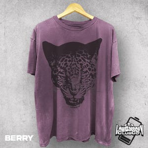 May include: Berry-colored t-shirt with a large black jaguar face graphic. The shirt is hanging on a wooden hanger against a gray background. The text "BERRY" is at the bottom left of the shirt. The "Low Battery Club Co" logo is at the bottom right.