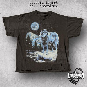 May include: A dark chocolate brown t-shirt with a graphic print of a wolf howling at the moon. The moon is blue and the wolf is white with blue accents. The background is a dark blue with stars.