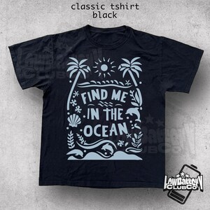 Puede incluir: Camiseta negra cl&aacute;sica con un gr&aacute;fico azul claro que dice "Find Me In The Ocean". El dise&ntilde;o incluye palmeras, un sol, olas, una concha y un delf&iacute;n. La camiseta es de corte cl&aacute;sico.