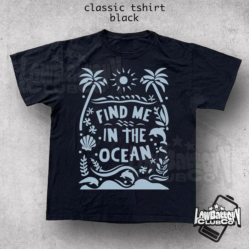 Puede incluir: Camiseta negra cl&aacute;sica con un gr&aacute;fico azul claro que dice "Find Me In The Ocean". El dise&ntilde;o incluye palmeras, un sol, olas, una concha y un delf&iacute;n. La camiseta es de corte cl&aacute;sico.