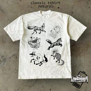 May include: A white, short-sleeved t-shirt with black fox illustrations. The shirt features the text "classic tshirt natural" at the top. A logo is visible at the bottom right corner.