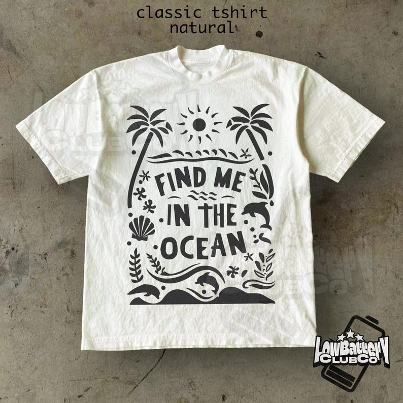 Puede incluir: Una camiseta cl&aacute;sica de color natural con un dise&ntilde;o gr&aacute;fico negro. El dise&ntilde;o presenta palmeras, un sol, olas, una concha y el texto "FIND ME IN THE OCEAN". La camiseta tiene mangas cortas y cuello redondo.