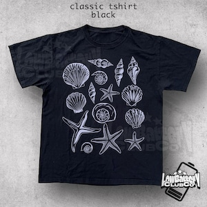 May include: Black classic t-shirt featuring a white illustration of various seashells and starfish. The shirt has the text "classic tshirt black" at the top. A logo is visible at the bottom right.