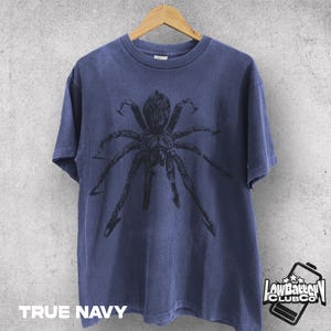 May include: True navy blue t-shirt featuring a large black spider graphic. The shirt is hanging on a wooden hanger against a neutral background. The text "TRUE NAVY" is printed at the bottom of the shirt.