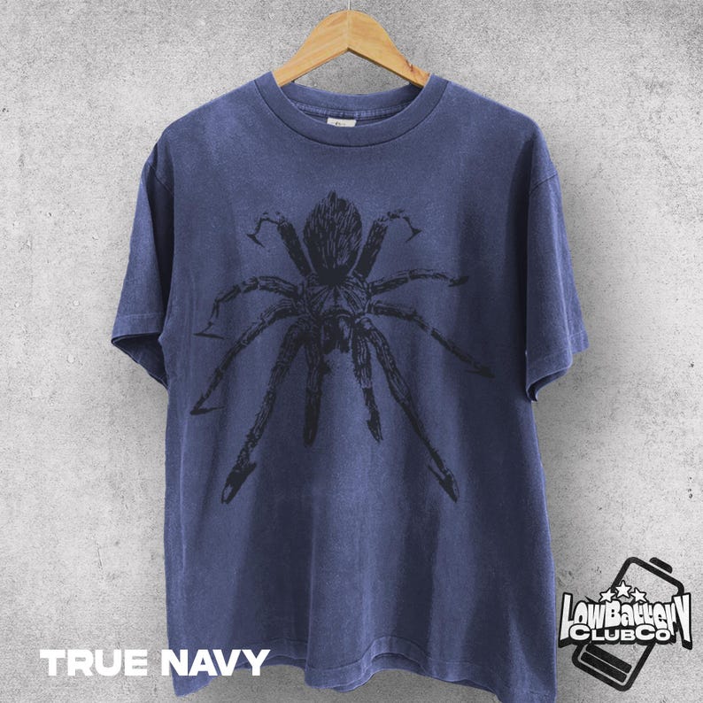 May include: True navy blue t-shirt featuring a large black spider graphic. The shirt is hanging on a wooden hanger against a neutral background. The text "TRUE NAVY" is printed at the bottom of the shirt.